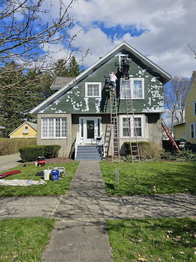 Exterior house painting in progress with ladders, painters, and prepared siding